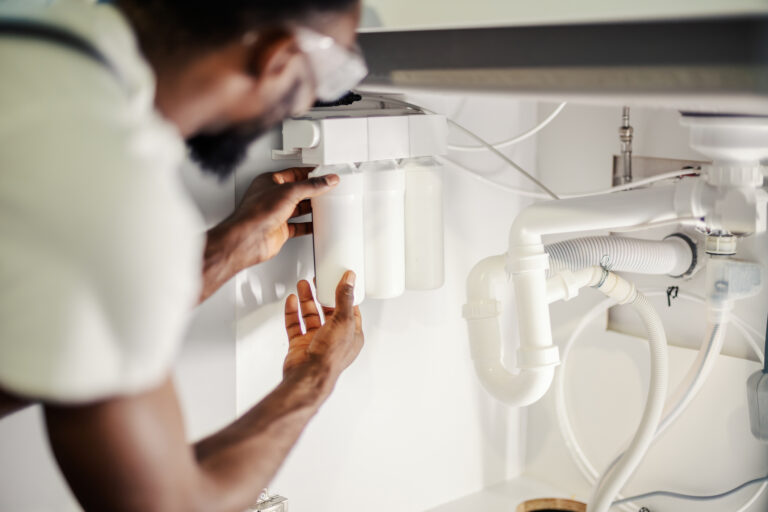 Professional plumber hands installing a multi-stage water filtration system under a kitchen sink, ensuring clean drinking water and home plumbing maintenance